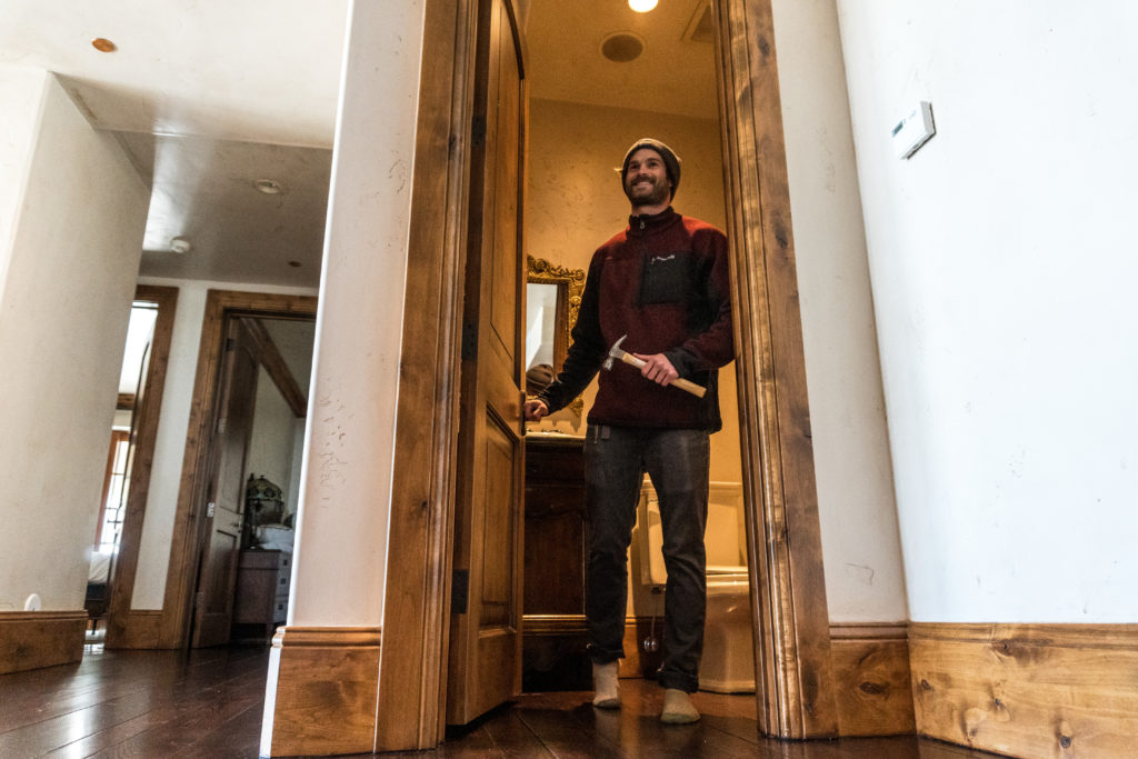 A man smiles holding a hammer and walking out of a bathroom