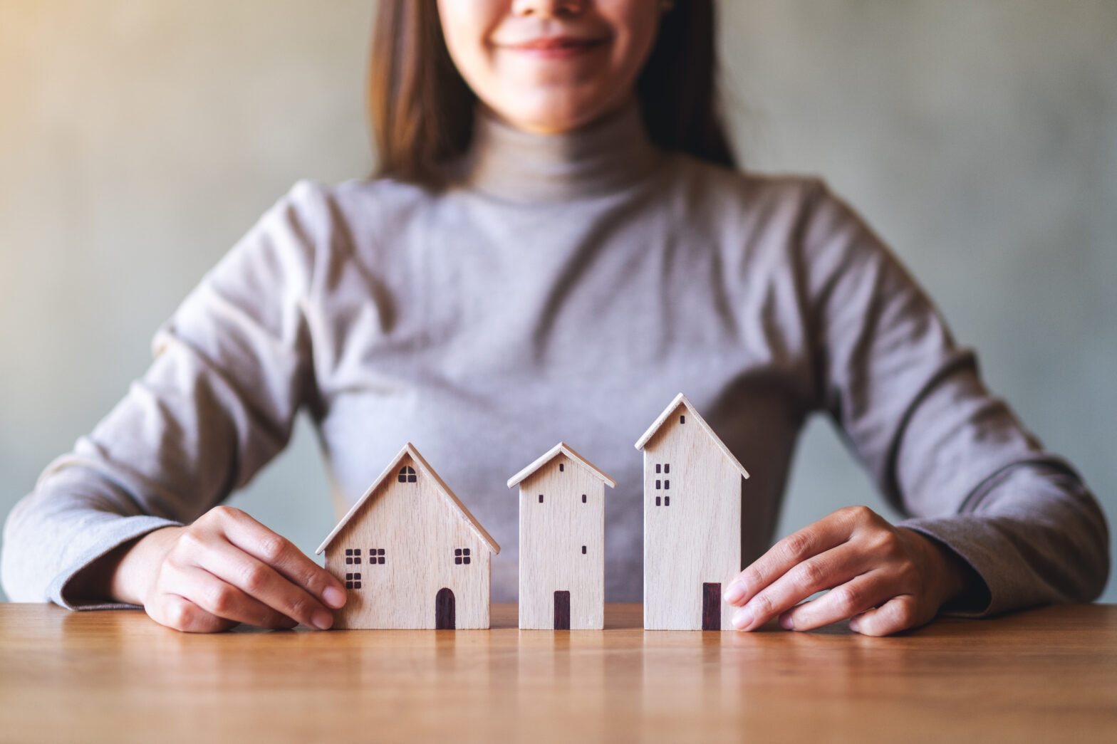 Property manager - Closeup image of a woman holding wooden house models on the table